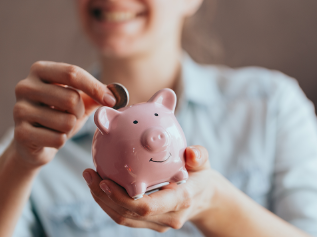 Eine Person hält ein Sparschwein und eine Münze in der Hand